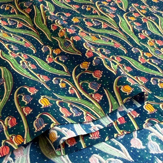 a close-up view of a fabric with a repeating pattern of colorful flowers and leaves, including lily of the valley flowers, against a dark background.