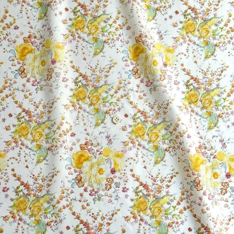 a close-up view of a fabric with a floral pattern. The fabric is predominantly white, adorned with yellow and orange flowers and leaves. The pattern repeats across the fabric, creating a visually appealing and vibrant design.