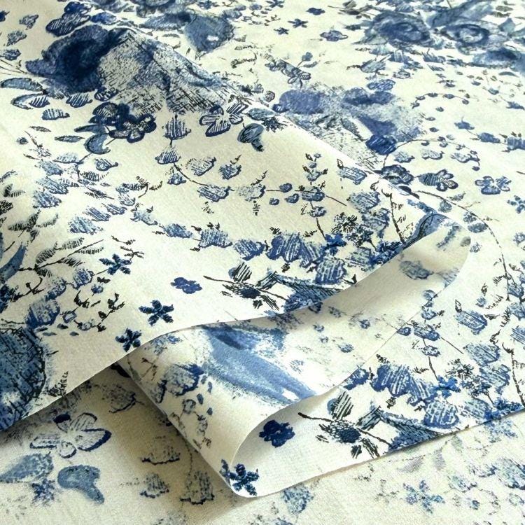 a close-up view of a fabric with a blue floral pattern. The fabric appears to be folded or rolled, revealing the intricate design of the blue flowers and leaves.