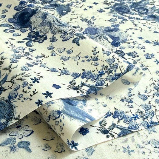 a close-up view of a fabric with a blue floral pattern. The fabric appears to be folded or rolled, revealing the intricate design of the blue flowers and leaves.