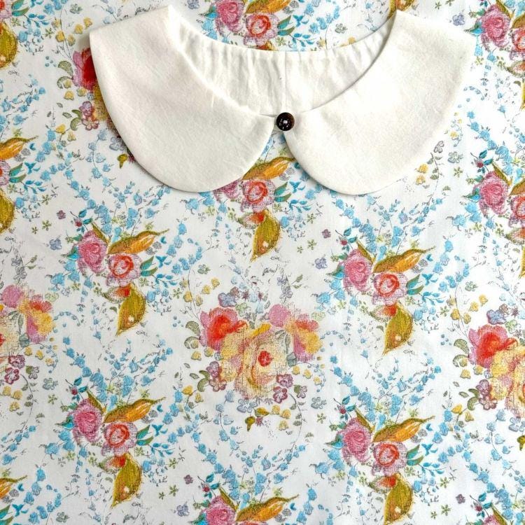 a white collar with a button, set against a background with a floral print.