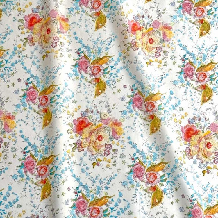 a close-up view of a fabric with a floral pattern. The fabric has a white background with a repeating pattern of colorful flowers and leaves in shades of pink, yellow, and green. The pattern is intricate and detailed, creating a visually appealing design.
