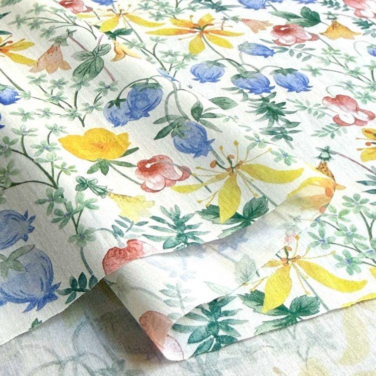 a close-up view of a fabric with a vibrant floral pattern. The fabric is adorned with a variety of colorful flowers, including yellow, blue, and pink blooms, as well as green leaves and stems. The pattern is intricate and detailed, showcasing the craftsmanship and artistry involved in creating the fabric.
