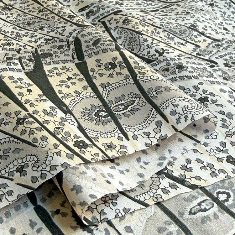 a close-up view of a fabric with a repeating pattern of black and white floral designs. The pattern is intricate and detailed, with the flowers and leaves arranged in a symmetrical and visually appealing manner. The fabric appears to be made of a soft, textured material, which adds to its overall aesthetic appeal.