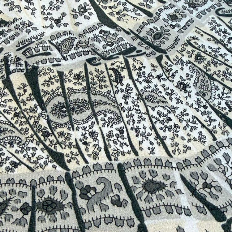 The image is a close-up of a fabric with a repeating pattern of black and white designs, including floral and geometric motifs.
