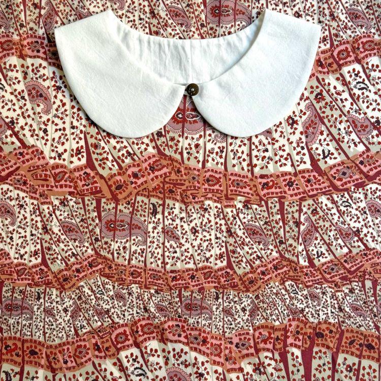 a white collar with a button, set against a background with a repeating pattern of red and white paisley designs.