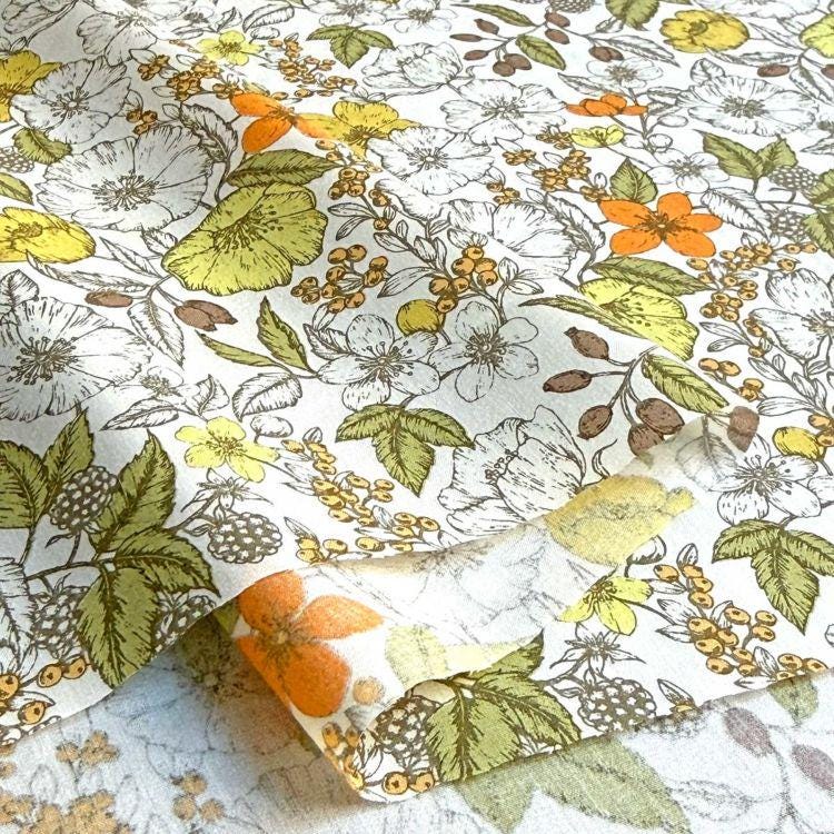 a close-up view of a fabric with a floral pattern, including various types of flowers and leaves in shades of yellow, orange, and green.