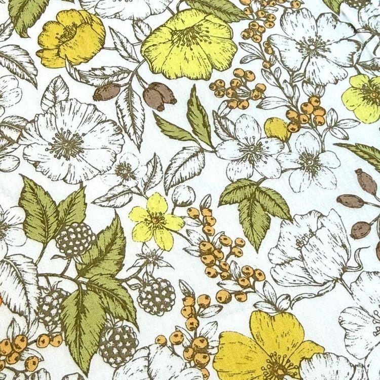 a close-up view of a white fabric adorned with a variety of colorful flowers and leaves, including yellow, white, and green hues. The flowers and leaves are intricately detailed, creating a visually appealing and textured pattern.