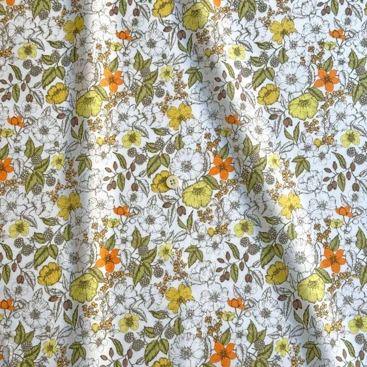 a close-up view of a fabric with a floral pattern. The fabric is predominantly white, with various shades of yellow, orange, and green flowers and leaves scattered across it. The pattern appears to be a repeating design, creating a visually appealing and textured appearance.