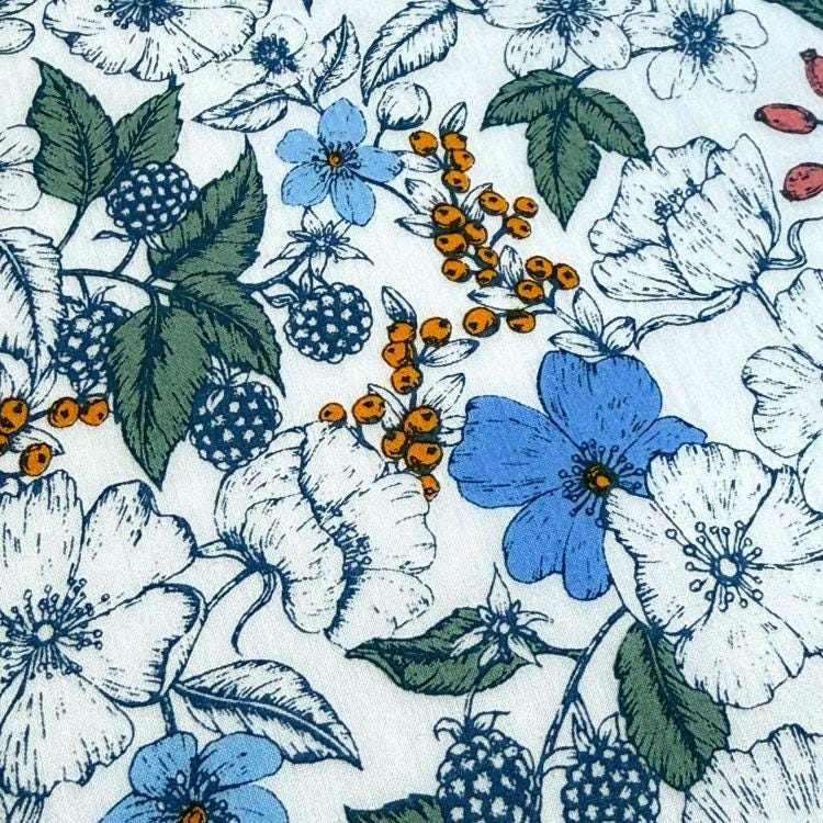 a close-up view of a fabric with a floral pattern. The pattern consists of various flowers and berries, including white, blue, and orange flowers, as well as green leaves and berries. The flowers and berries are arranged in a visually appealing manner, creating a vibrant and colorful design.