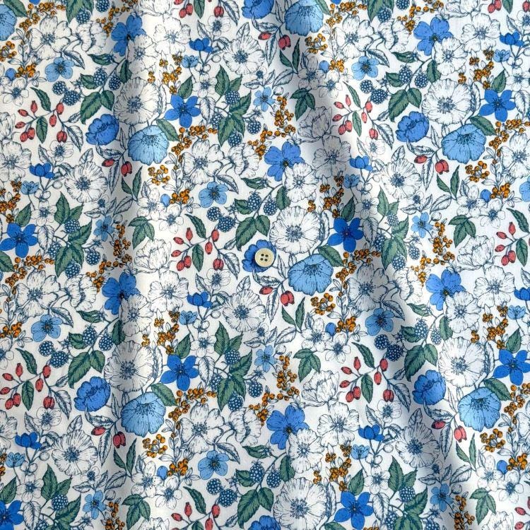 a close-up view of a fabric with a floral pattern in shades of blue, white, and orange. The pattern features various types of flowers and leaves, creating a vibrant and colorful design.