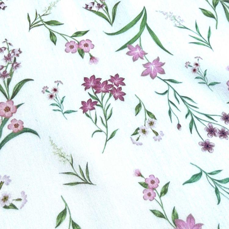 a close-up view of a white fabric adorned with a variety of pink and green floral designs. The designs include small flowers, leaves, and branches, creating a visually appealing and intricate pattern.