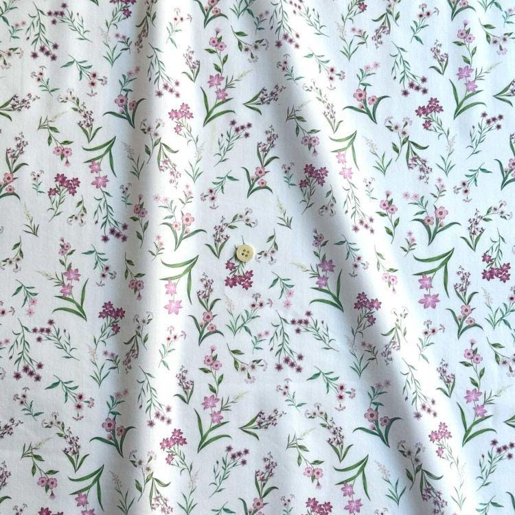 a close-up view of a fabric with a repeating floral pattern in shades of pink and green. The pattern consists of small flowers and leaves, creating a delicate and intricate design. The fabric appears to be made of a soft, white material, which contrasts with the vibrant colors of the flowers. The image does not contain any text or other objects, and the focus is solely on the floral pattern.