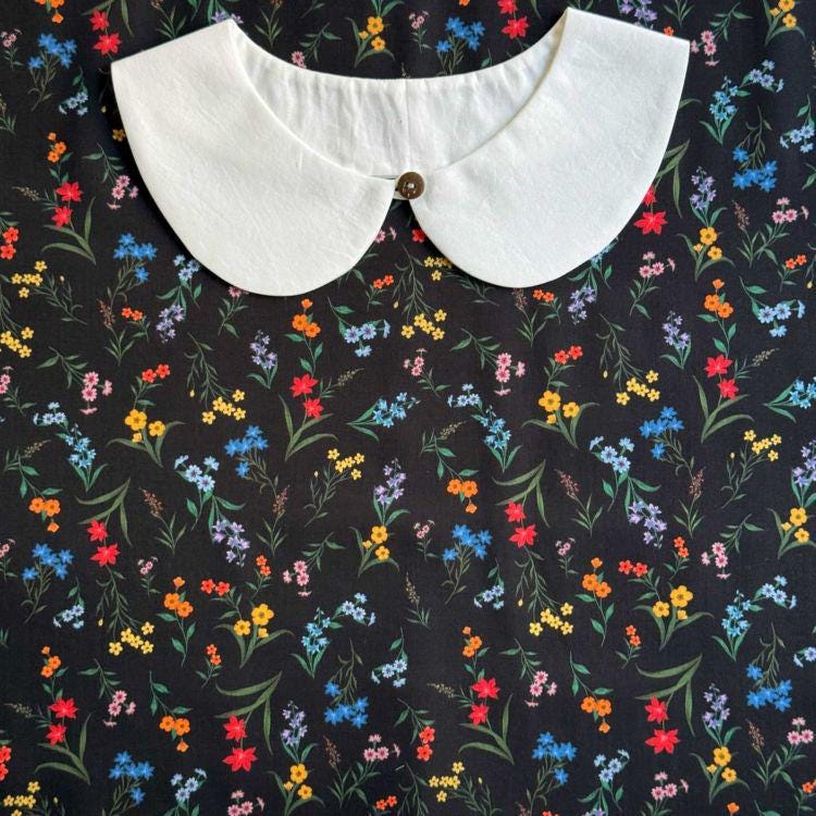 a white collar with a button, placed on a black fabric with a colorful floral pattern.