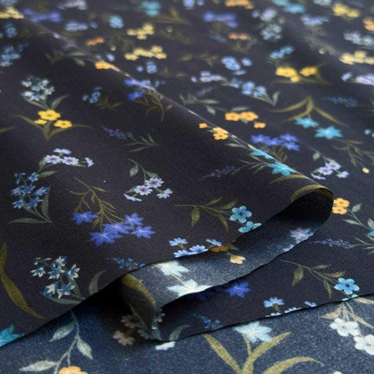 a close-up view of a fabric with a floral pattern in shades of blue, yellow, and white. The fabric appears to be folded or rolled, revealing the intricate design of the flowers and leaves.