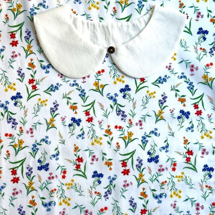 a white collar with a button, set against a background with a colorful floral print.