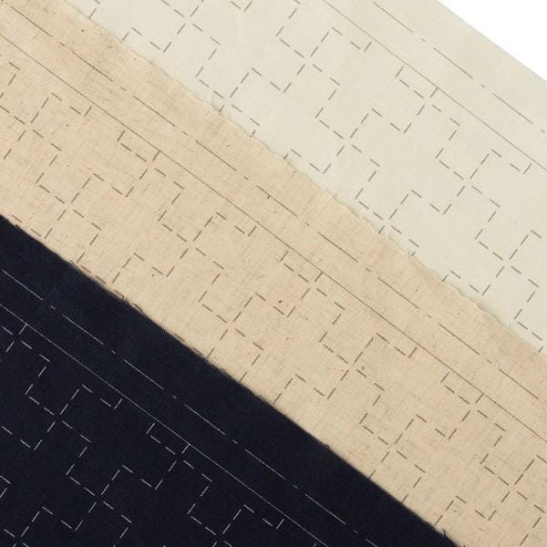 The image is a close-up of a fabric with a repeating pattern of squares and lines, with varying shades of beige and black.