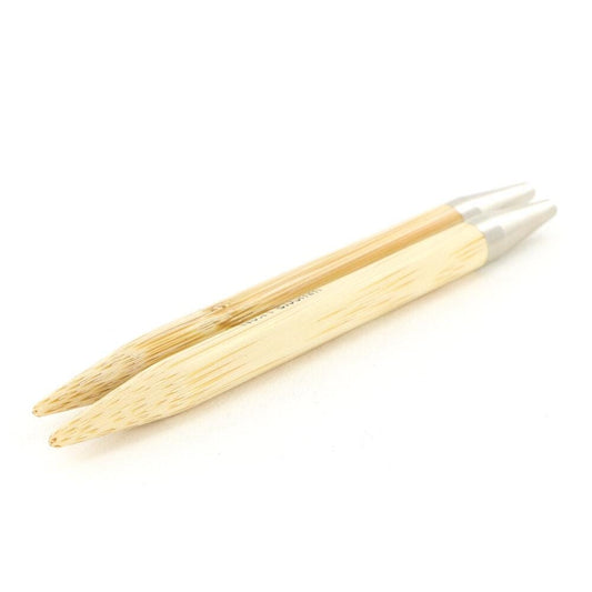 A pair of wooden knitting needles with silver tips, lying on a white background.