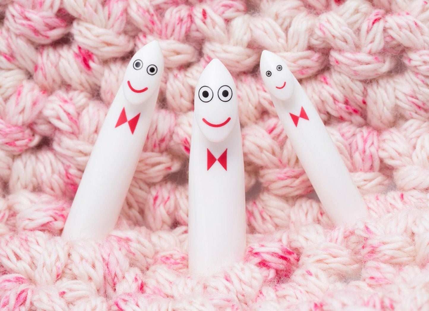 Three white crochet hooks with red bows and faces are arranged on a pink and white crocheted surface.
