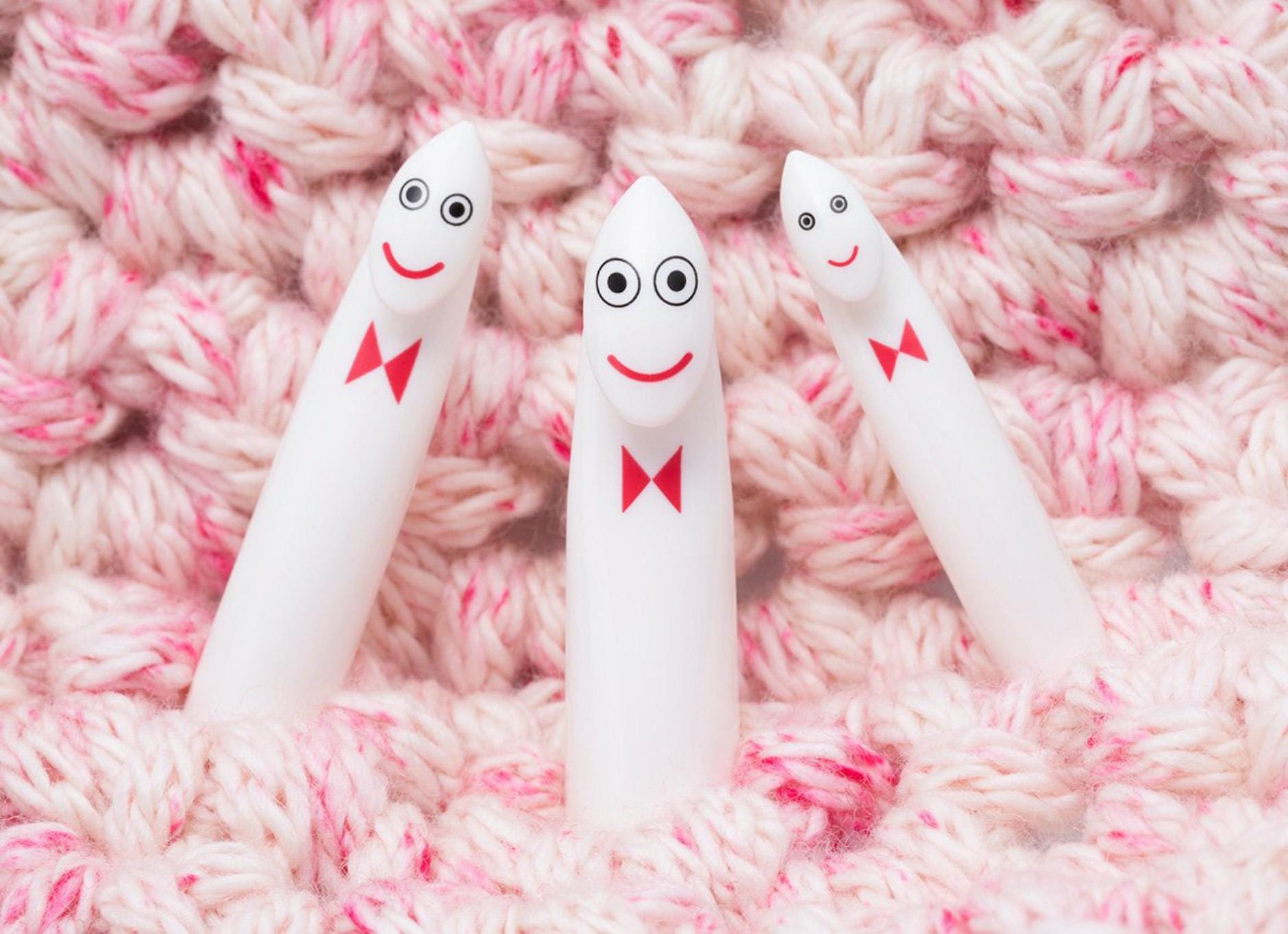 Three white crochet hooks with red bows and faces are arranged on a pink and white crocheted surface.