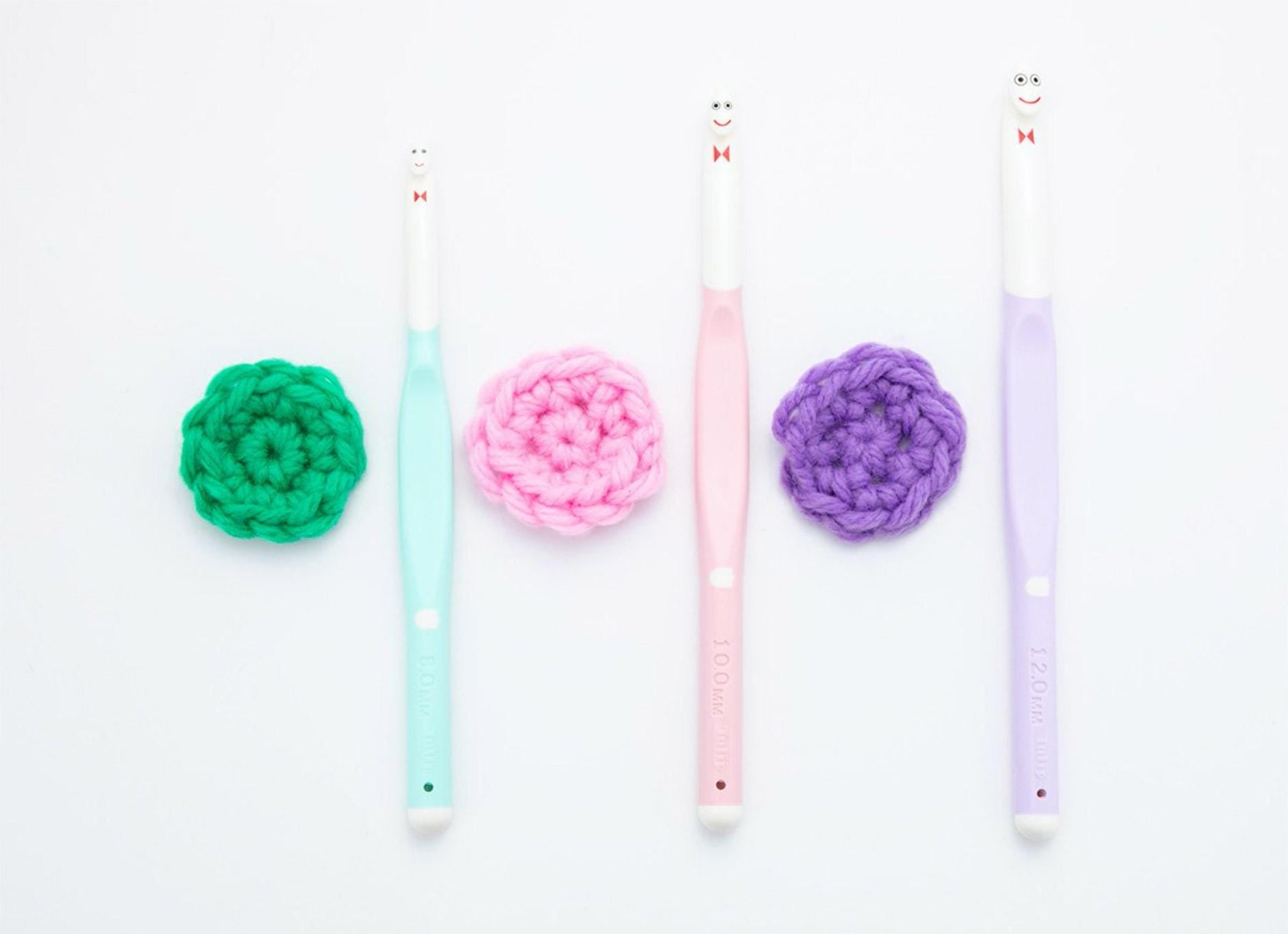 four crochet hooks of different colors arranged in a row on a white background.