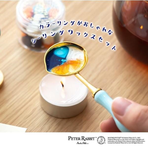 A hand holding a spoon with a colorful substance, possibly a sauce or syrup, in front of a lit candle on a wooden surface.