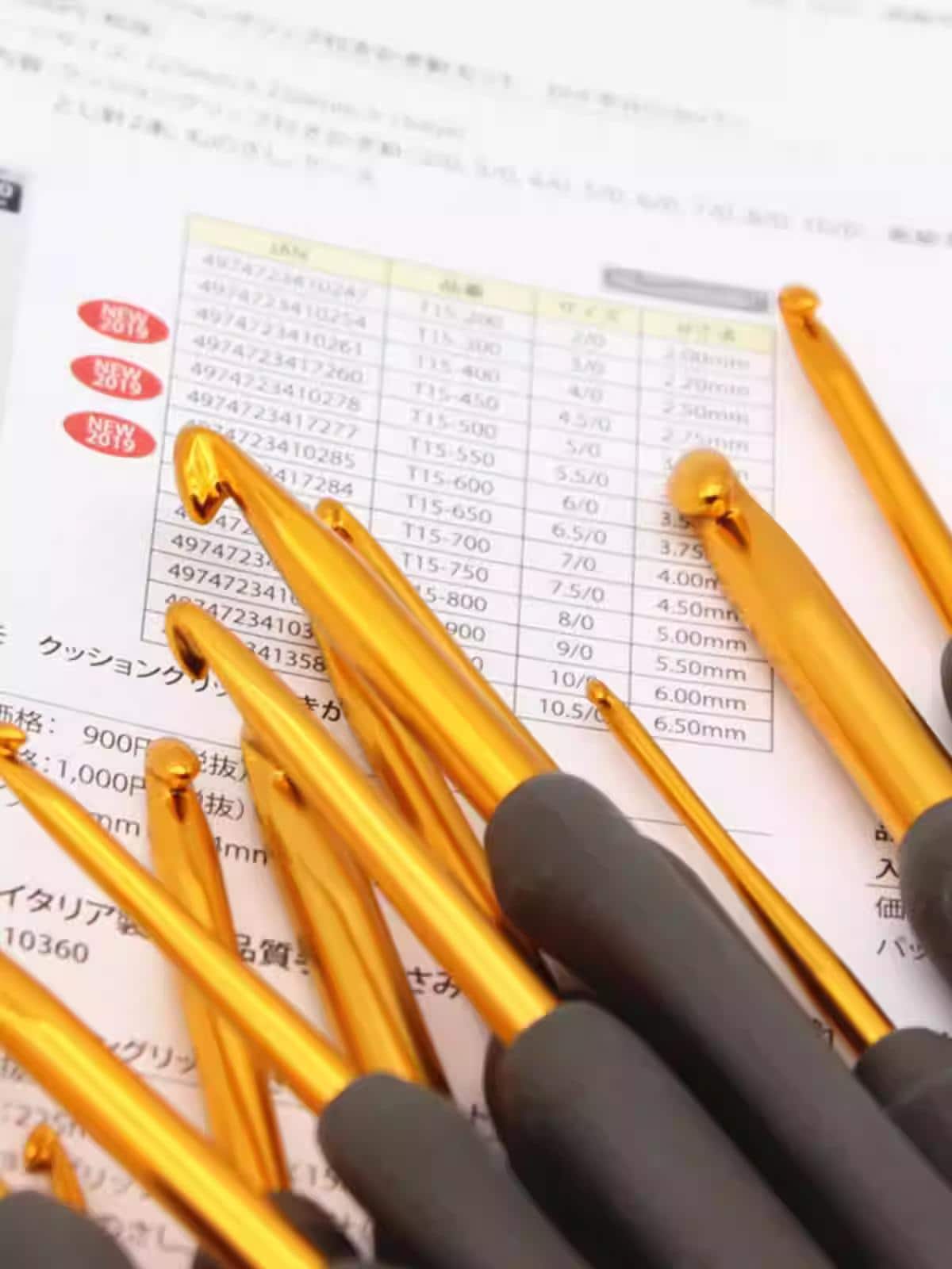 a collection of gold crochet hooks arranged on top of a sheet of paper with Japanese text, likely providing information about the hooks or their sizes.