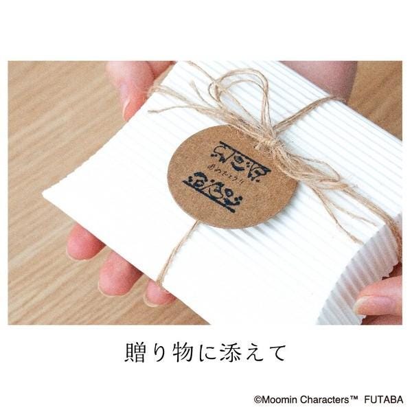 A person's hands holding a white paper with a brown circular tag featuring Japanese text.