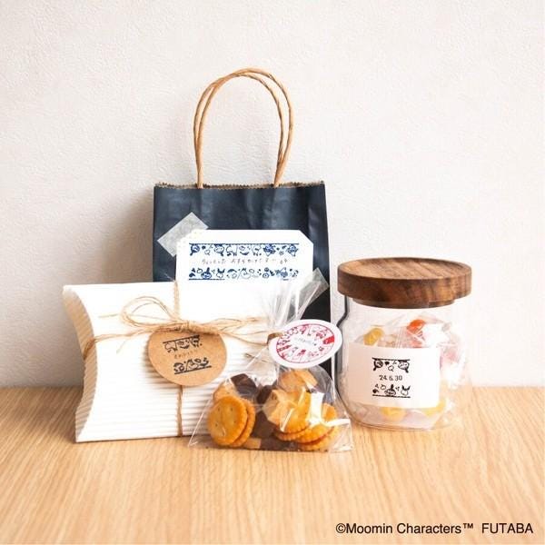 a variety of snacks and a gift bag on a wooden surface, including a jar of candy, a bag of cookies, and a small gift bag.