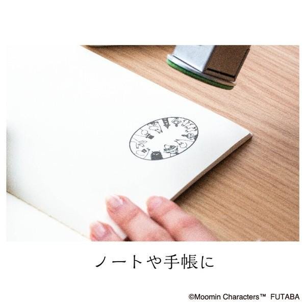 A hand is holding a piece of paper with a stamp featuring a circular design on it, placed on a wooden surface.