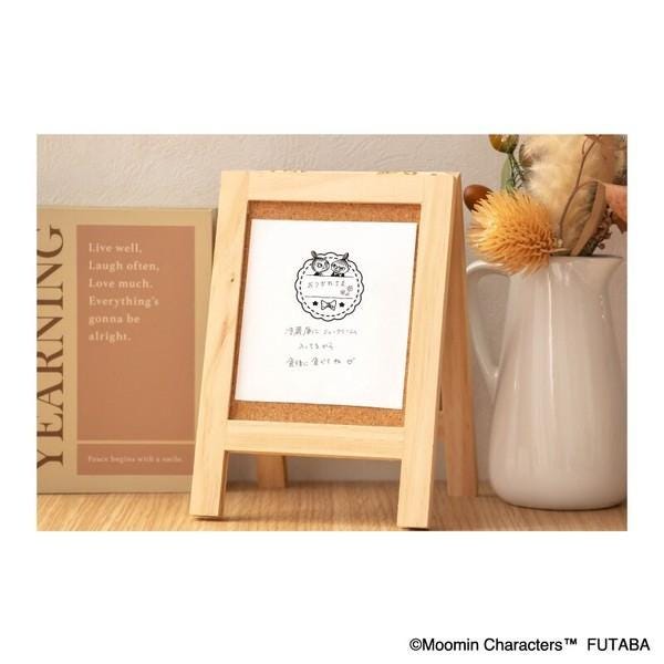 a wooden frame with a white paper inside, placed on a wooden surface next to a white ceramic pitcher and a brown book.