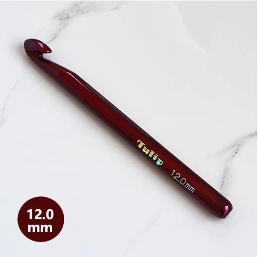 A red crochet hook with the word "Tulip" printed on it, lying on a white marble surface.