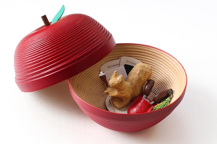 A red bowl with a lid, containing various small objects, including a wooden toy and a small figurine.