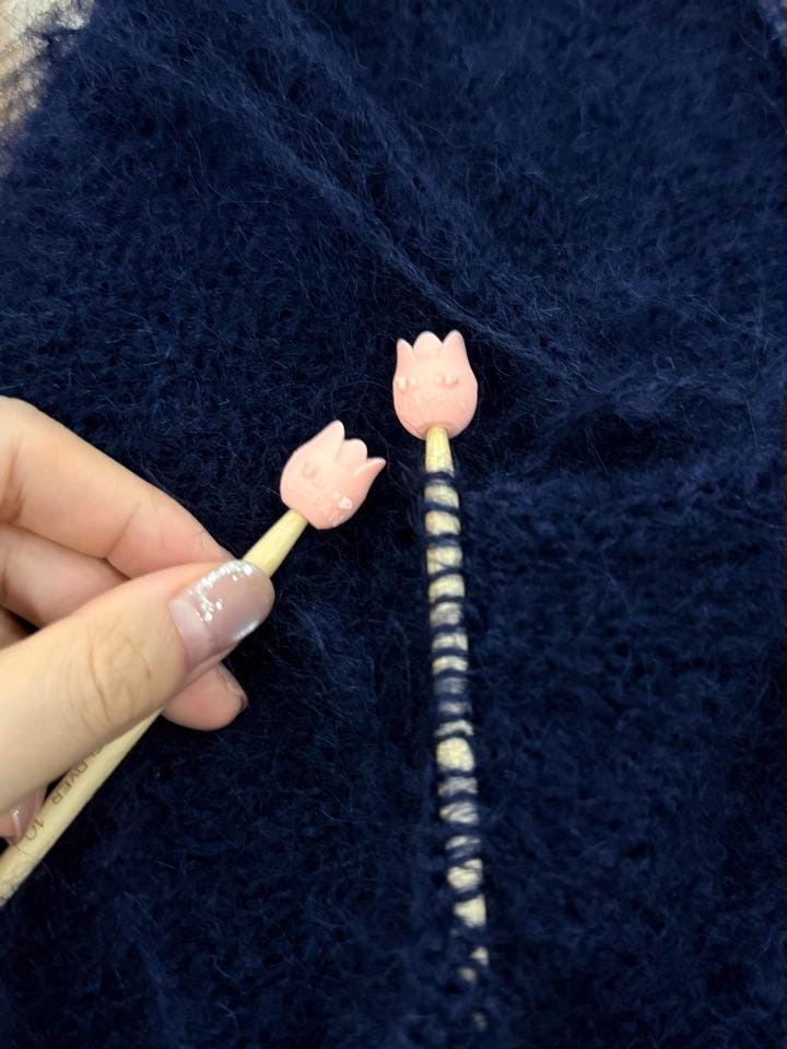 A hand holding two pink flower-shaped objects with black stems against a navy blue background.