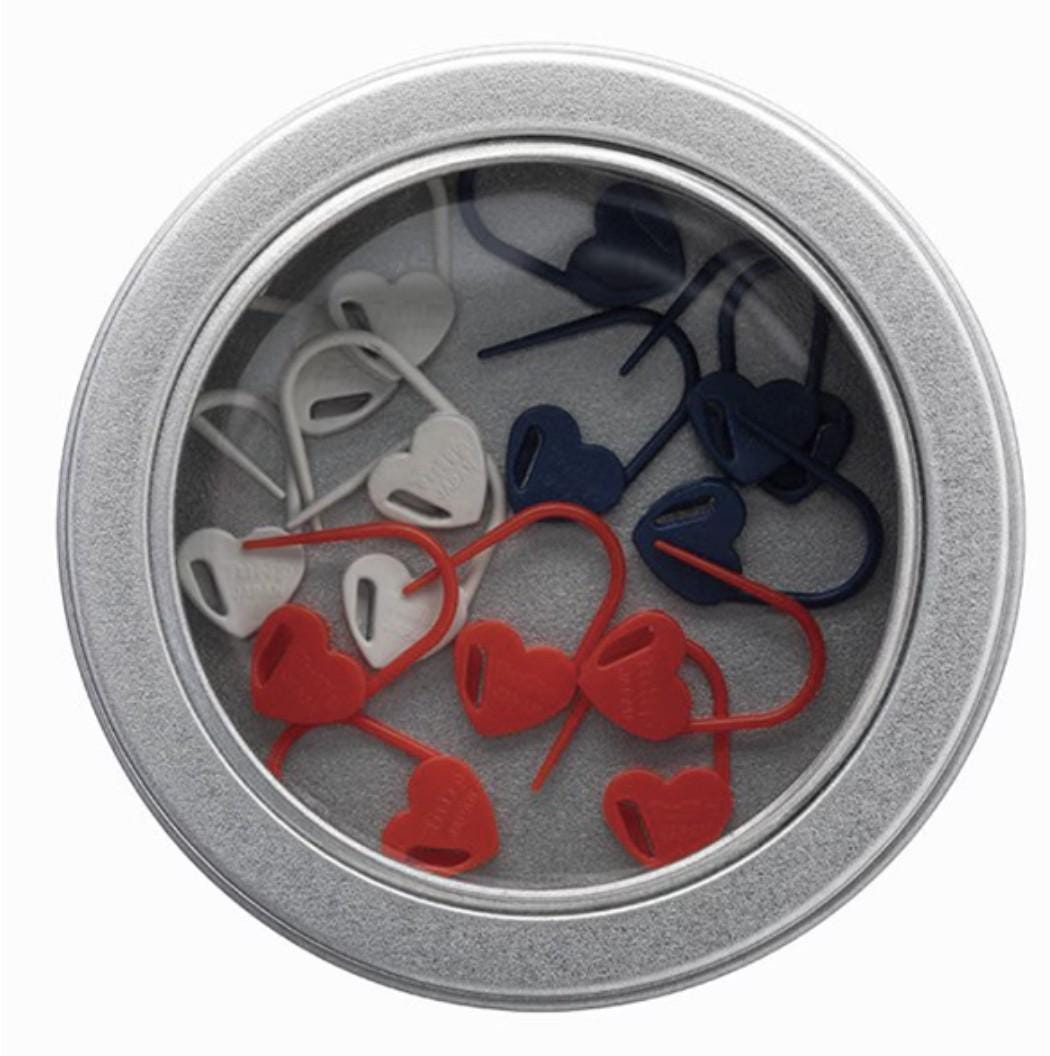 A round tin can containing a collection of heart-shaped objects, including red and white hearts and blue hearts, arranged in a circular pattern.