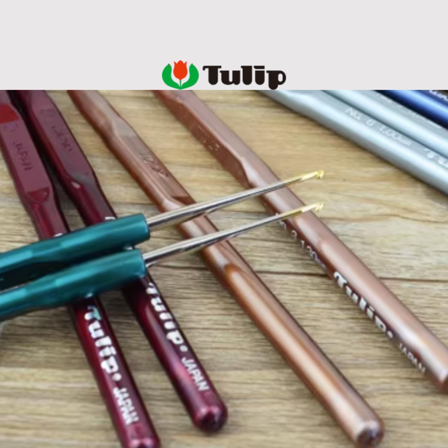 A collection of crochet hooks in various colors, including red, green, and brown, arranged on a wooden surface.