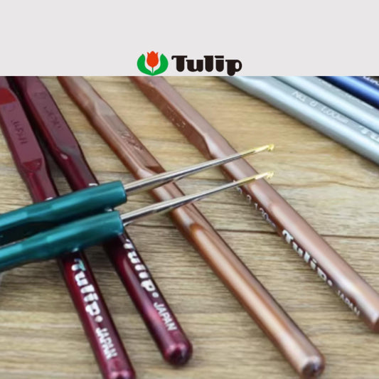 A collection of crochet hooks in various colors, including red, green, and brown, arranged on a wooden surface.