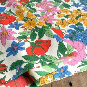 a vibrant and colorful floral pattern, with various flowers and leaves in shades of red, yellow, blue, and pink. The pattern appears to be a printed fabric or textile, with the flowers and leaves arranged in a visually appealing and intricate manner.
