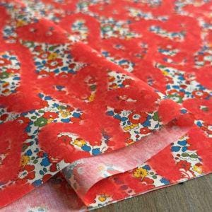 a close-up view of a vibrant red fabric with a floral pattern. The fabric appears to be folded or rolled, revealing its intricate design.