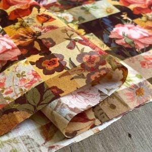 a close-up view of a fabric with a floral pattern, including various shades of pink, red, and yellow flowers. The fabric appears to be folded or rolled up, showcasing the intricate design and vibrant colors.