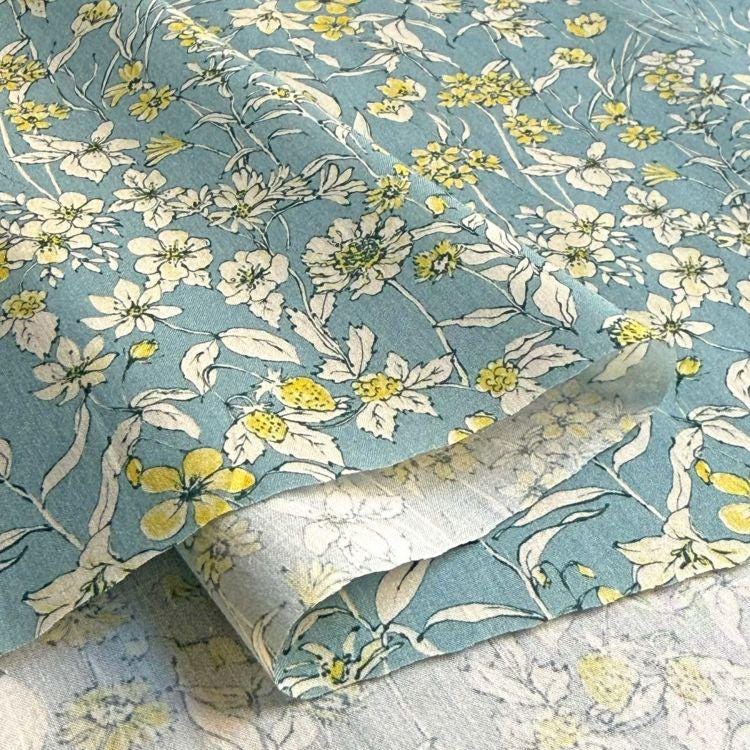 a close-up view of a fabric with a floral pattern in shades of blue and yellow. The fabric appears to be a piece of cloth or textile, with the pattern consisting of various flowers and leaves in different sizes and colors. The overall appearance of the fabric is visually appealing and suggests it could be used for clothing or home decor items.