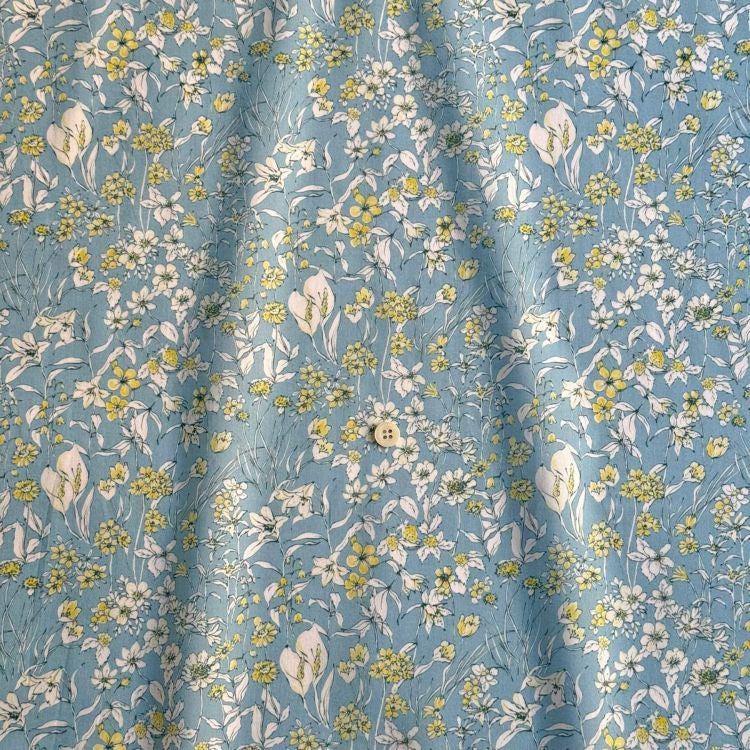 a close-up view of a fabric with a floral pattern in shades of blue and yellow. The pattern consists of various flowers and leaves, creating a vibrant and lively design. The fabric appears to be made of a soft, textured material, suitable for clothing or home decor.