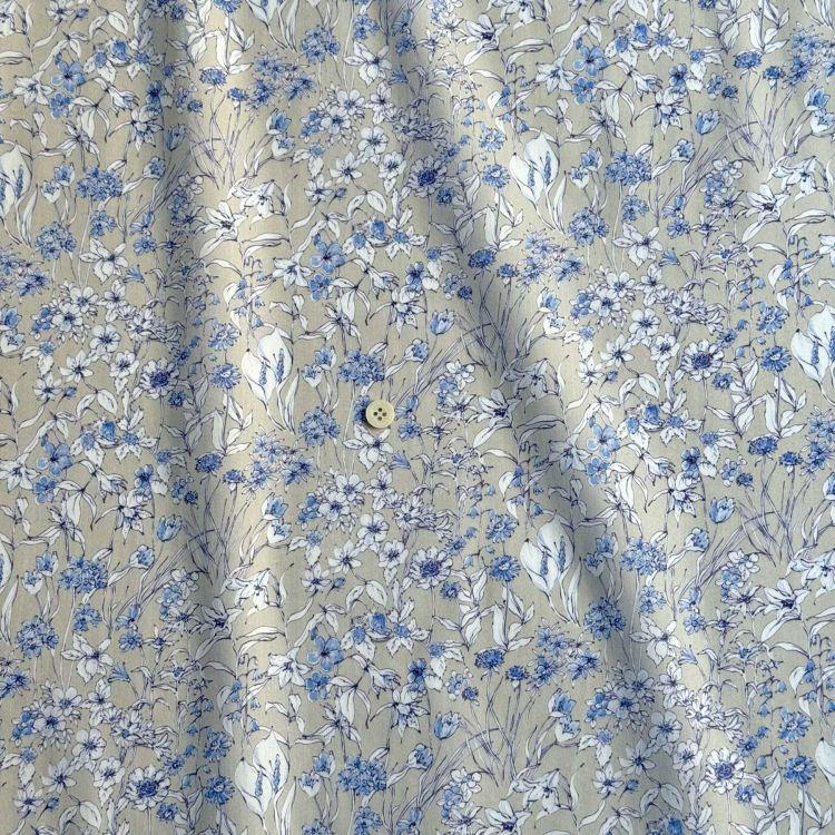 a close-up view of a fabric with a floral pattern in shades of blue and white. The fabric appears to be made of a soft, light-colored material, possibly cotton or linen. There is a small button visible in the center of the fabric.