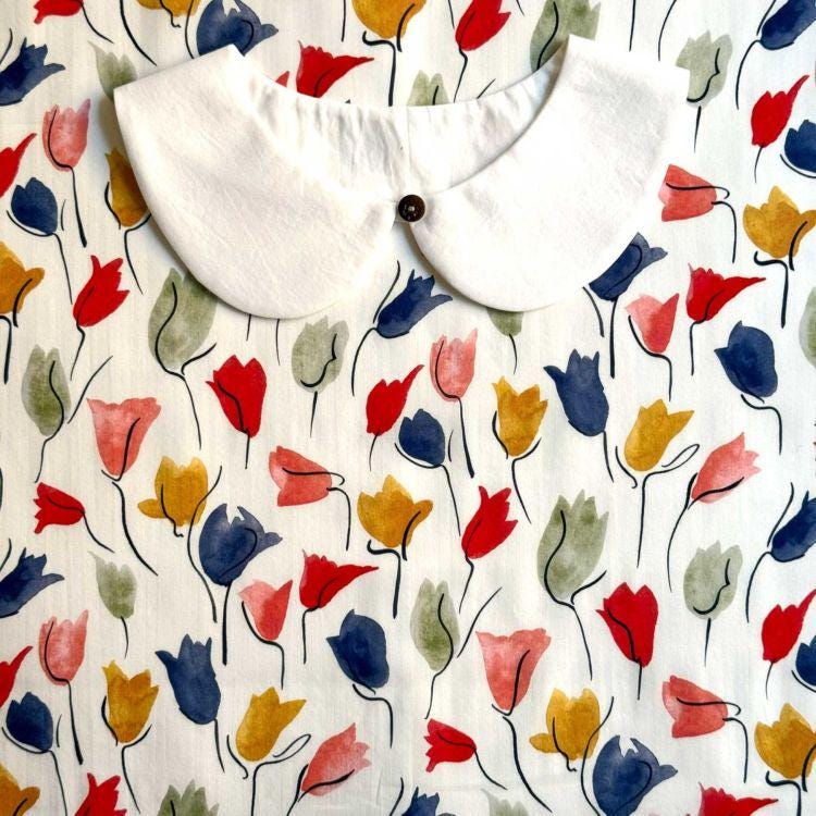a white collar with a button, set against a background with a repeating pattern of colorful flowers in various shades of red, yellow, blue, and green.