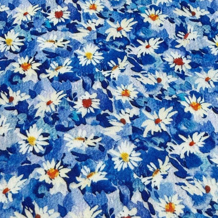The image is a close-up of a fabric with a vibrant blue and white floral pattern. The pattern consists of numerous white flowers with orange centers, creating a visually striking and colorful design. The fabric appears to be a textile or material with a textured surface, adding depth and dimension to the overall appearance.