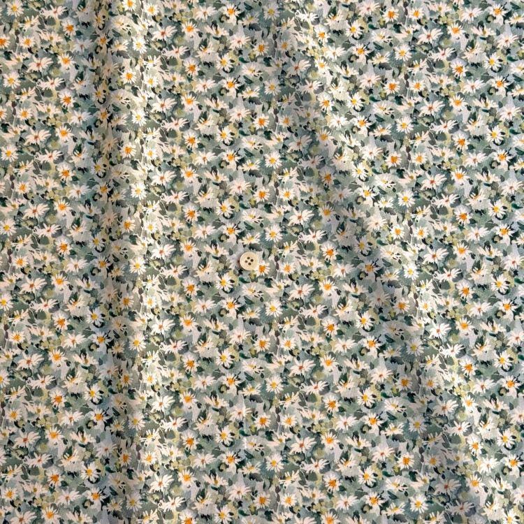 a fabric with a floral pattern, featuring a variety of white and green flowers. The fabric appears to be made of a soft, light-colored material, and there is a small button visible in the center of the fabric.