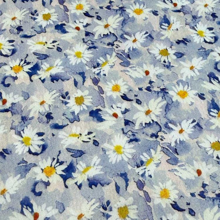 a close-up view of a fabric with a repeating pattern of white and blue daisy flowers. The daisies are arranged in a scattered manner, creating a visually appealing and textured appearance.