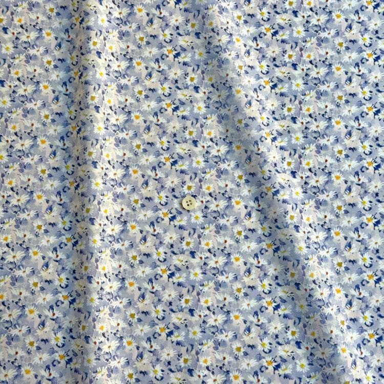 a close-up view of a fabric with a blue and white floral pattern. The fabric appears to be made of a soft, flowy material, and there is a small button visible in the center of the fabric.