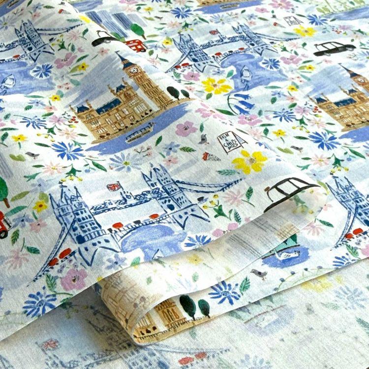 The image is a close-up of a fabric with a floral pattern featuring various landmarks and cityscapes, including London landmarks such as Big Ben, the Tower Bridge, and the Houses of Parliament.