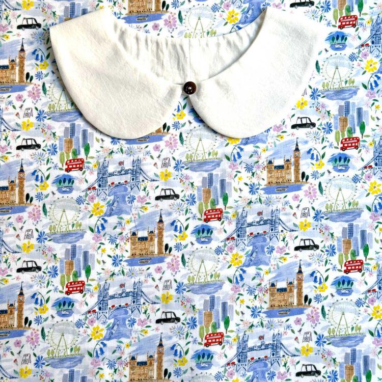 a white collar with a button, set against a background with a repeating pattern of various landmarks and cityscapes, including London landmarks such as Big Ben, the London Eye, and the Houses of Parliament.